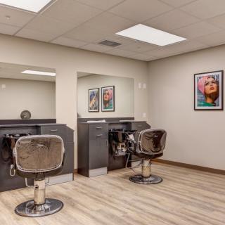 A modern hair salon with two styling stations featuring comfortable chairs, large mirrors, and vibrant wall art.
