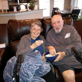 An elderly couple relaxing with a bowl of popcorn in their living room.