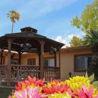 A charming house with a wooden gazebo and colorful flowers in the garden under a clear blue sky.