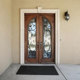 A set of elegant wooden double doors with decorative glass and wrought iron designs, accompanied by an exterior light fixture and a doormat.
