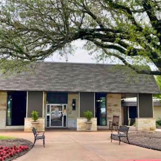 A charming building surrounded by lush trees and colorful flowers, featuring outdoor seating.