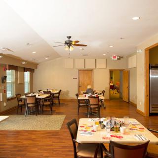 A dining area with multiple tables and chairs, featuring a wooden floor and ceiling fan.