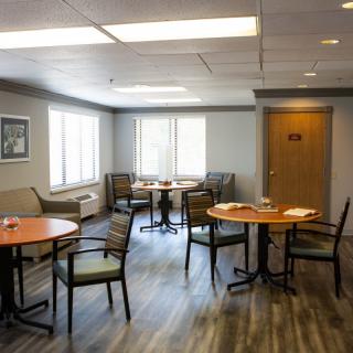 A modern lounge area with tables and chairs, featuring large windows and ample lighting.