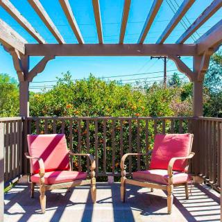 A sunny patio with two red chairs under a wooden pergola.