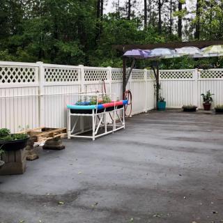 An outdoor patio with a white fence, potted plants, and colorful umbrellas.