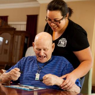 An elderly man receiving supportive care from a caregiver, both enjoying the moment.