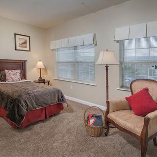 Cozy bedroom with a bed, chair, and large windows.