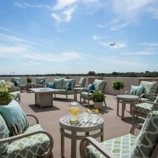 A spacious outdoor patio with comfortable seating and a clear blue sky, featuring a plane flying overhead.