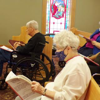 Elderly individuals participating in a communal reading during a religious service.