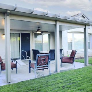 A cozy patio area with comfortable seating under a pergola, adjacent to a well-maintained lawn.