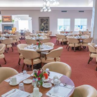 A well-arranged dining area with multiple set tables and chairs, featuring bright natural lighting.