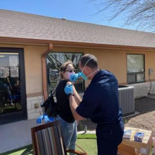 A healthcare professional administering a vaccination to a patient outdoors, both wearing masks for safety.