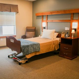 A cozy hospital room featuring a bed, nightstand, and comfortable seating.