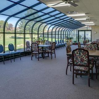 A spacious conservatory with large windows and several tables and chairs under a glass ceiling.