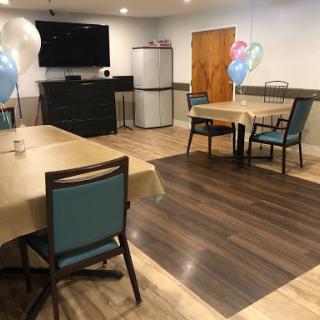 A cozy dining area with tables and chairs, decorated with balloons, featuring a television and a refrigerator in the background.