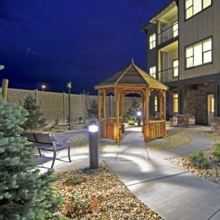 A well-lit garden with a gazebo and pathway at night, next to a building.