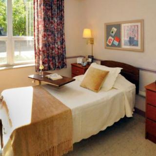 A cozy bedroom with a single bed, side drawers, and a window letting in natural light.