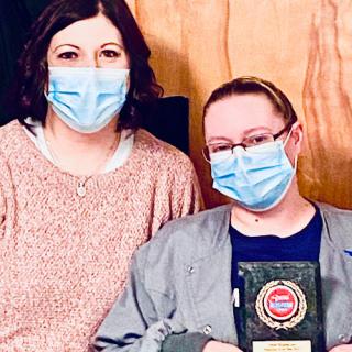 Two individuals proudly holding an award while wearing masks.