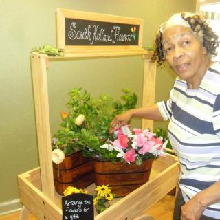 A woman standing beside a small flower market display indoors.