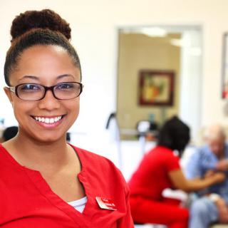 A smiling woman in a red uniform inside a medical setting.