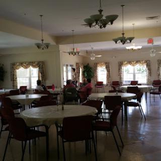 A spacious community dining area with round tables and chairs, illuminated by ceiling lights.
