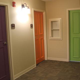 A hallway featuring three colorful doors in purple, orange, and green.