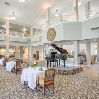 An elegant and spacious dining area featuring a grand piano and neatly arranged tables with white tablecloths.