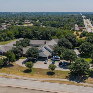 An aerial view of a suburban area featuring a large building surrounded by trees and vehicles in the parking lot.