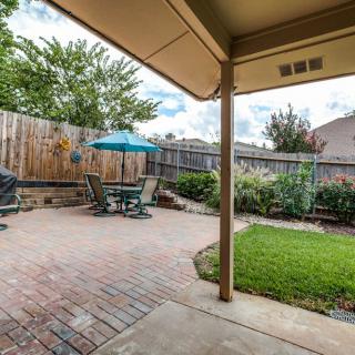 A cozy backyard with a brick patio, featuring outdoor furniture and an umbrella, surrounded by greenery.