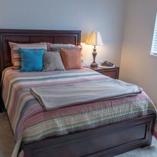 A cozy bedroom with a neatly made bed featuring striped bedding and assorted pillows, accompanied by a nightstand and lamp.