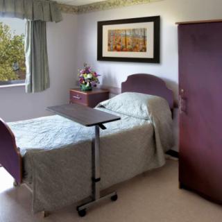 A well-organized hospital room with a single bed, an overbed table, and a window with curtains.