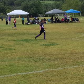 A youth soccer game in progress, with players and spectators under tents on a grassy field.