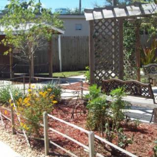 A beautifully landscaped garden featuring a pergola with outdoor seating and various plants.