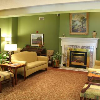 A cozy living room with green walls, featuring a fireplace, sofa, and comfortable seating.