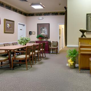 A conference room with a large table surrounded by chairs, decorated with artwork, plants, and a piano.