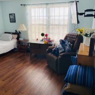 A cozy bedroom with an armchair, bed, and desk by a large window.