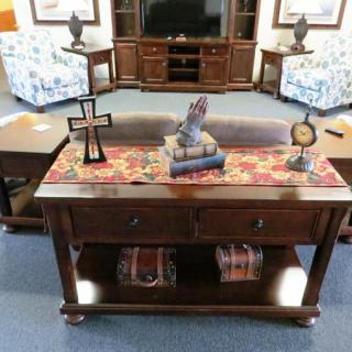 A living room featuring a wooden console table adorned with decorative items including a cross, books, a sculpture, and a clock.