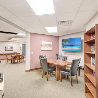 An office meeting room with a conference table, chairs, bookshelf, and artwork on the walls.