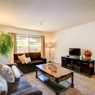 A cozy living room featuring a comfortable sofa, a coffee table, and a TV stand, illuminated by natural light.