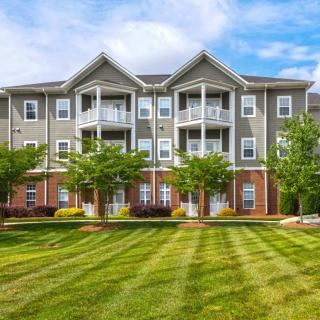A well-maintained apartment building with a manicured lawn and trees in front.