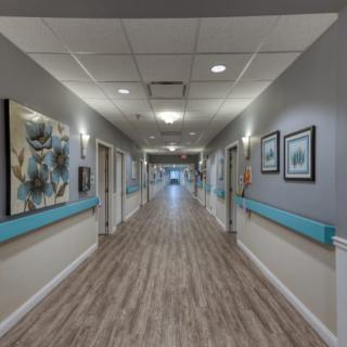 A long, well-lit hallway with paintings on the walls and wood-style flooring.