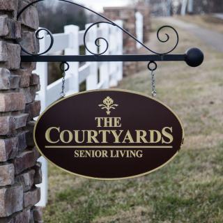 An outdoor sign for 'The Courtyards Senior Living' mounted on a brick wall.