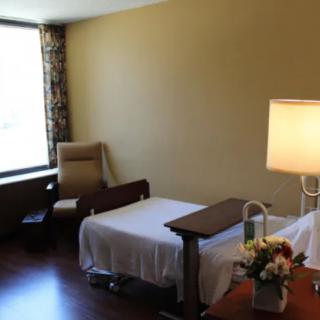 A hospital room with a bed, chair, and lamp, featuring a large window with curtains.
