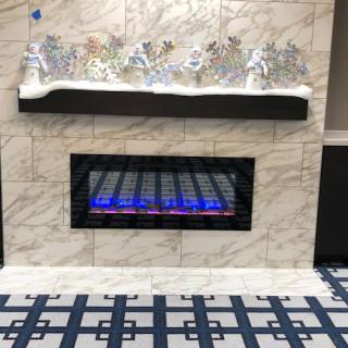 An electric fireplace set into a marble wall, adorned with festive holiday decorations on the mantelpiece.