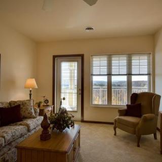A cozy living room with a sofa, armchair, and coffee table, warmly lit by a lamp and natural light from the windows.