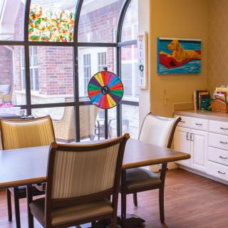 A cozy room with a table and chairs, featuring a colorful wheel and artwork on the wall.