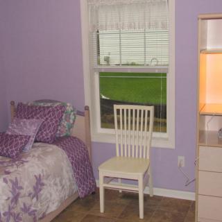 A cozy bedroom with purple walls, a bed, and a chair by the window.