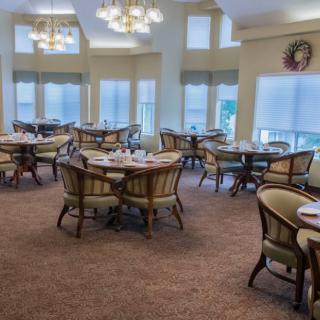 A spacious dining room with elegantly arranged tables and chairs, featuring chandeliers and large windows.