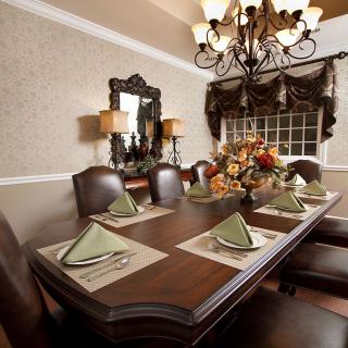 A beautifully set dining room with an elegant table, adorned with folded napkins and a floral centerpiece, under a classic chandelier.