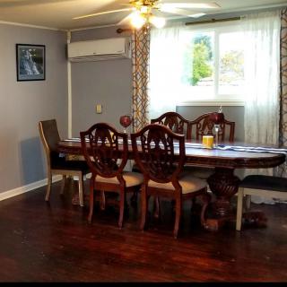 A cozy dining room with a wooden table and chairs, featuring a ceiling fan and natural light from the window.